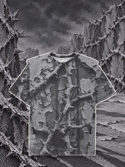 La t-shirt grigia Bloodrose Dark, con un bordo di carta chiara, fra muri di rovi grigi in rilievo.