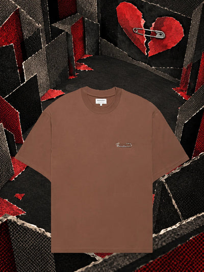 La t-shirt marrone Brokenheart in una stanza di carta scura, sotto un cuore di carta rossa spezzato in due.