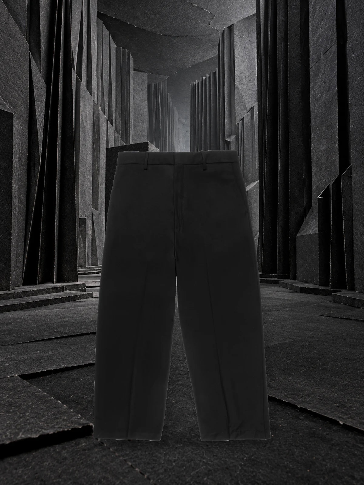 The black Classic trousers standing in a corridor of black paper folded into deep pleats, with grey light at the far end.