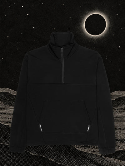 La felpa a mezza zip nera Eclipse su dune di carta nera, sotto un'eclissi con un anello di luce bianca.