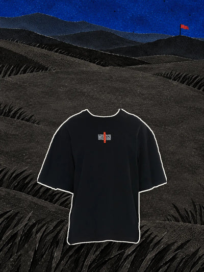 La t-shirt nera Flag con l'etichetta rossa sul petto, sopra colline di carta nera sotto un cielo blu di notte.