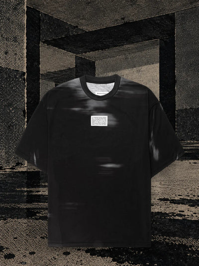 La t-shirt nera Leak in una stanza di carta scura, con l'inchiostro nero che cola sul pavimento in lunghe strisce.