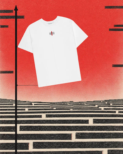 La Manifesto T-Shirt bianca, con la piccola toppa e il nastro rosso sul petto, legata per un lato a un'asta nera come una bandiera, contro un cielo rosso a retino. Sotto, una pianura fatta di file di barre nere su carta chiara, e altre barre nere che galleggiano nel cielo.