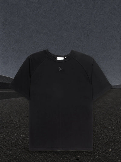La t-shirt raglan nera Minimal su una piana di carta nera, con la nebbia di carta chiara all'orizzonte.