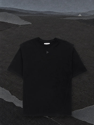La t-shirt nera Minimal SP su una piana di carta nera quasi vuota, sotto un cielo di carta grigio scuro.