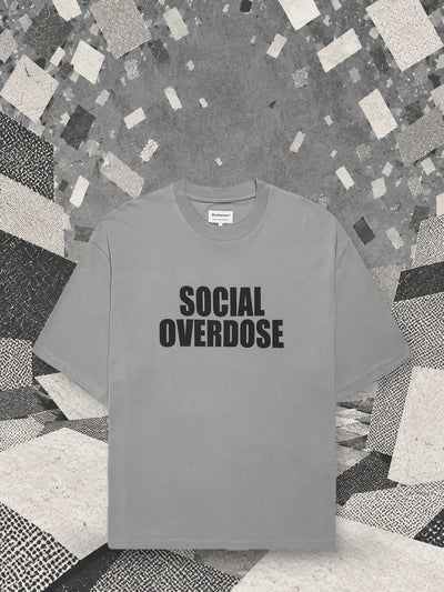 La t-shirt grigia Social Overdose sotto una nevicata di piccoli cartoncini bianchi e grigi, su un paesaggio di blocchi di carta.