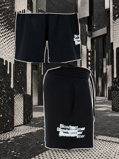 The black Stencil bermuda shorts with the white spray lettering, seen from the back hanging on a thread and from the side, in a black paper alley marked with white.
