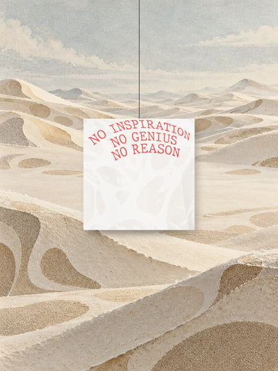 Et kvadrat klippet ud af trykket fra Strand Ivory sweatshirten, med den røde skrift NO INSPIRATION NO GENIUS NO REASON, hængt i en tråd over klitter af elfenbensfarvet papir.
