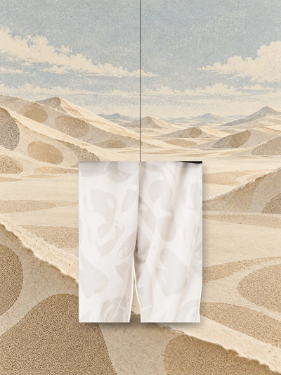 Un pezzo della stampa dei joggers avorio Strand Ivory, appeso a un filo sopra dune di carta color sabbia.