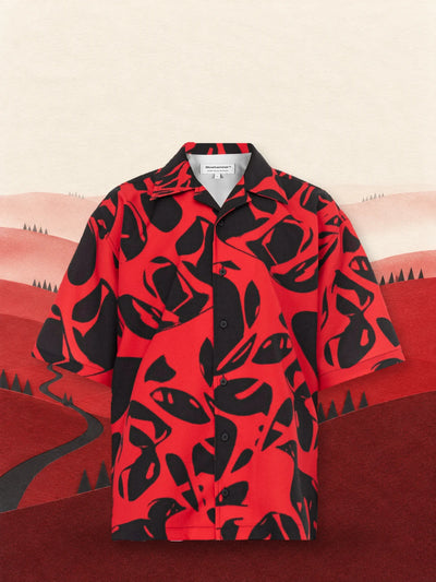 La camicia a maniche corte rossa e nera Strand Red fra colline di carta rossa, sotto un cielo chiaro.