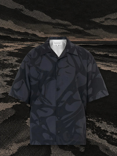 La camicia a maniche corte nera Strand sulla riva di un fiume di carta nera, sotto un cielo scuro.