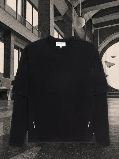 The black Travel Agency long sleeve t-shirt in a grey paper waiting room, with paper planes hanging in front of a large porthole.