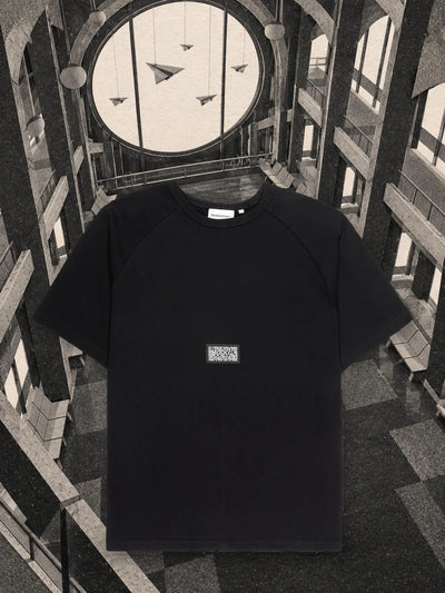 La t-shirt nera Travel Agency in una sala d'attesa di carta, con aeroplani di carta appesi davanti a un grande oblò.