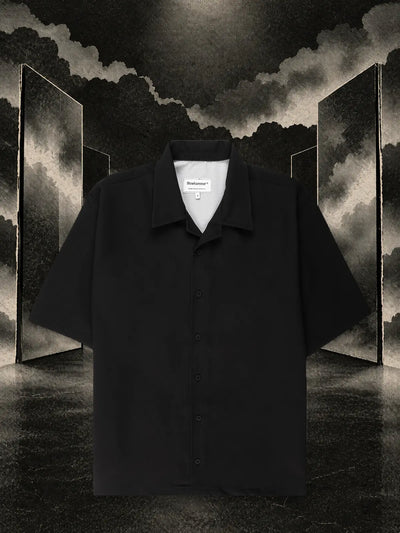 La camicia a maniche corte nera Triodrome fra pannelli di carta scura riflessi nell'acqua, nella nebbia.