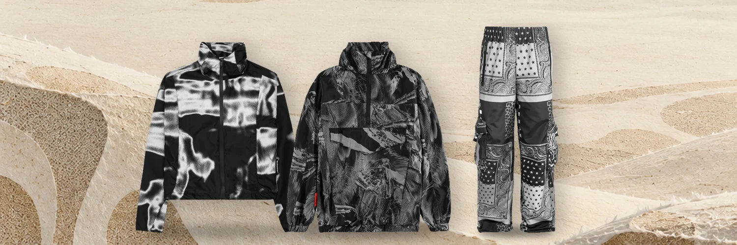The Rift windbreaker, the Insectide Vision anorak and the Romanticbandana cargo trousers in a row on ivory paper dunes.